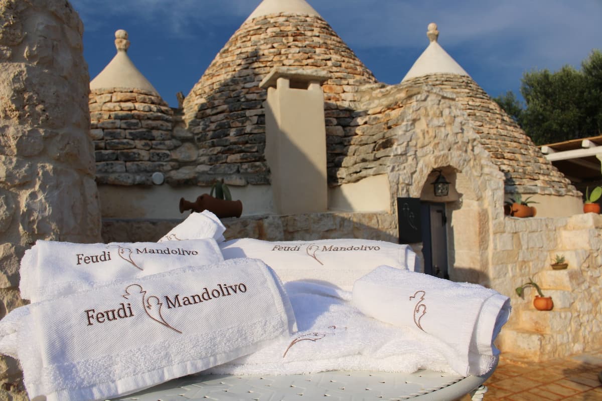 A stone-roofed building with three conical roofs, a door, and a small window. There are towels with the name "Feudi Mandolivo" on them.