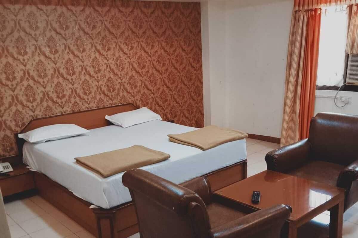 Una habitación de hotel con dos camas, un sofá, una mesa de centro y una ventana con cortinas.
