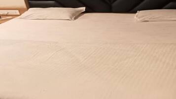 Cama com lençol branco e duas almofadas, cabeceira de madeira e mesa de cabeceira com abajur.