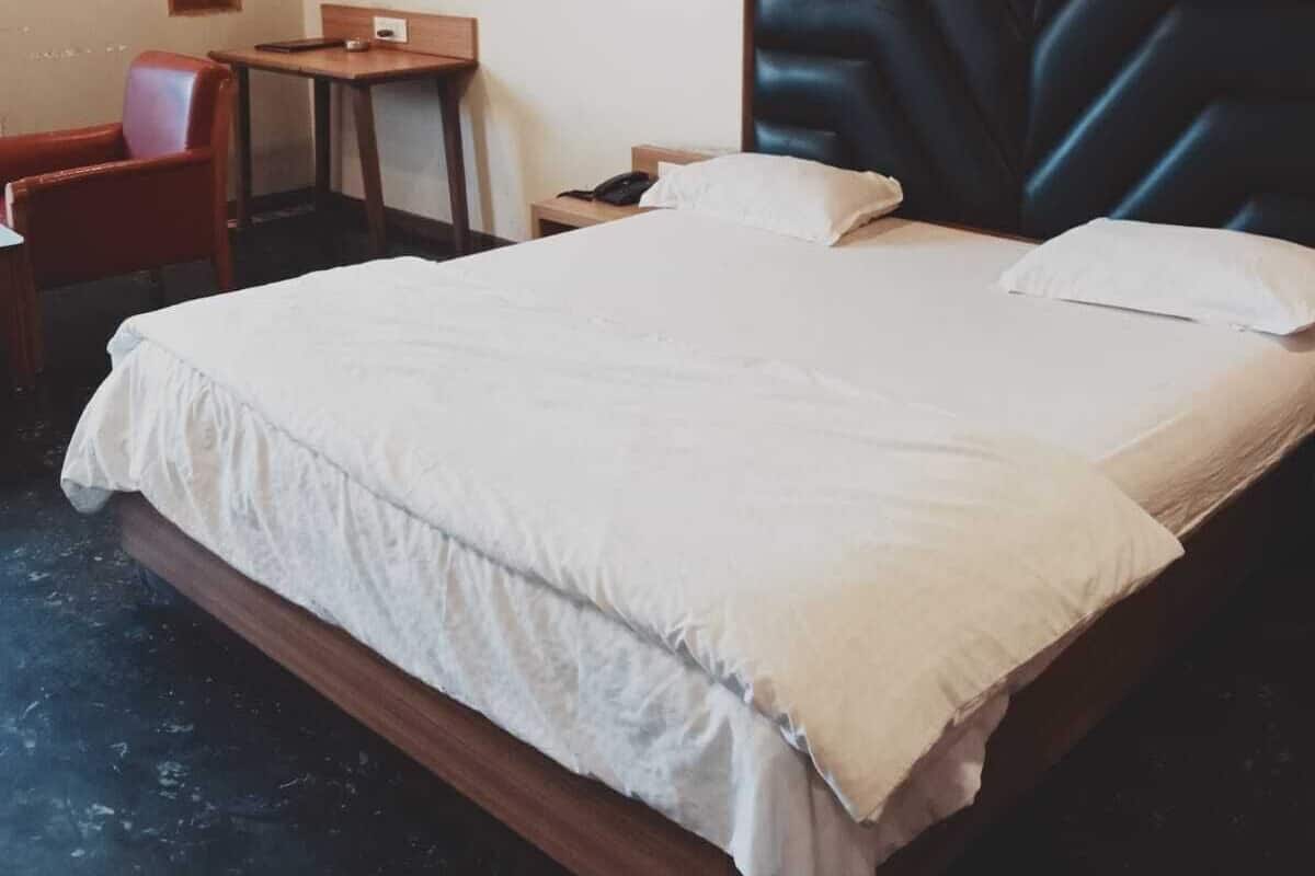 Un cuarto de hotel con una cama grande, un cabecero de madera, un escritorio pequeño, una silla y un espejo redondo en la pared.