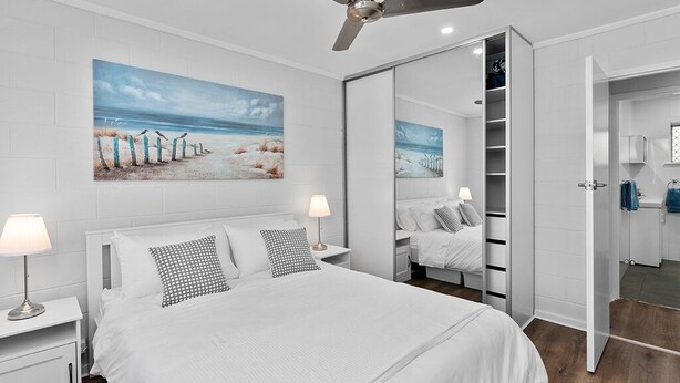 Un dormitorio moderno con una cama grande, un ventilador de techo, una mesita de noche con lámpara, un armario y un espejo.