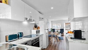 Una cocina moderna con armarios blancos, horno empotrado y comedor con mesa y sillas.