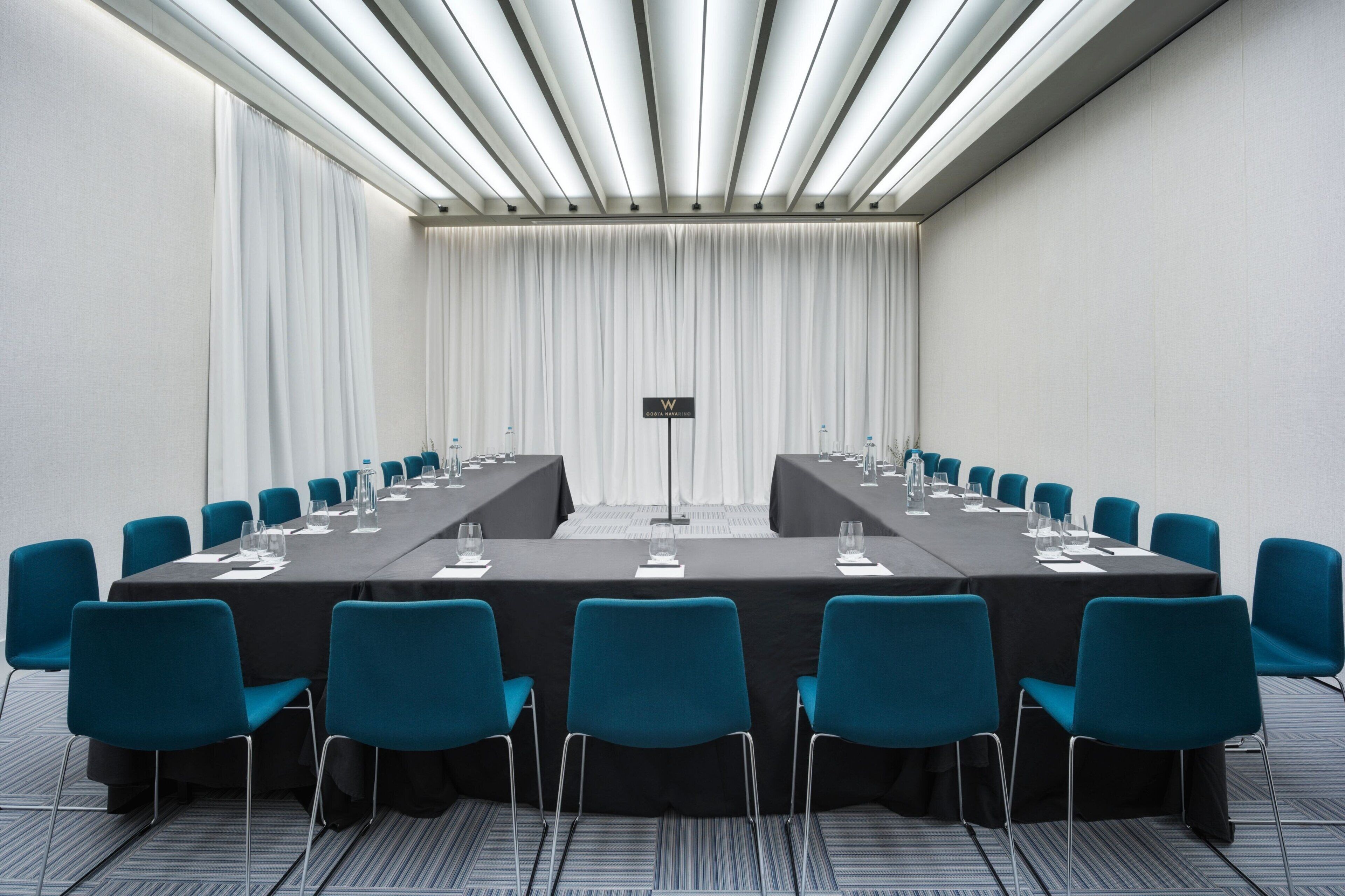 A conference room with a long table, blue chairs, and a sign indicating the room number.