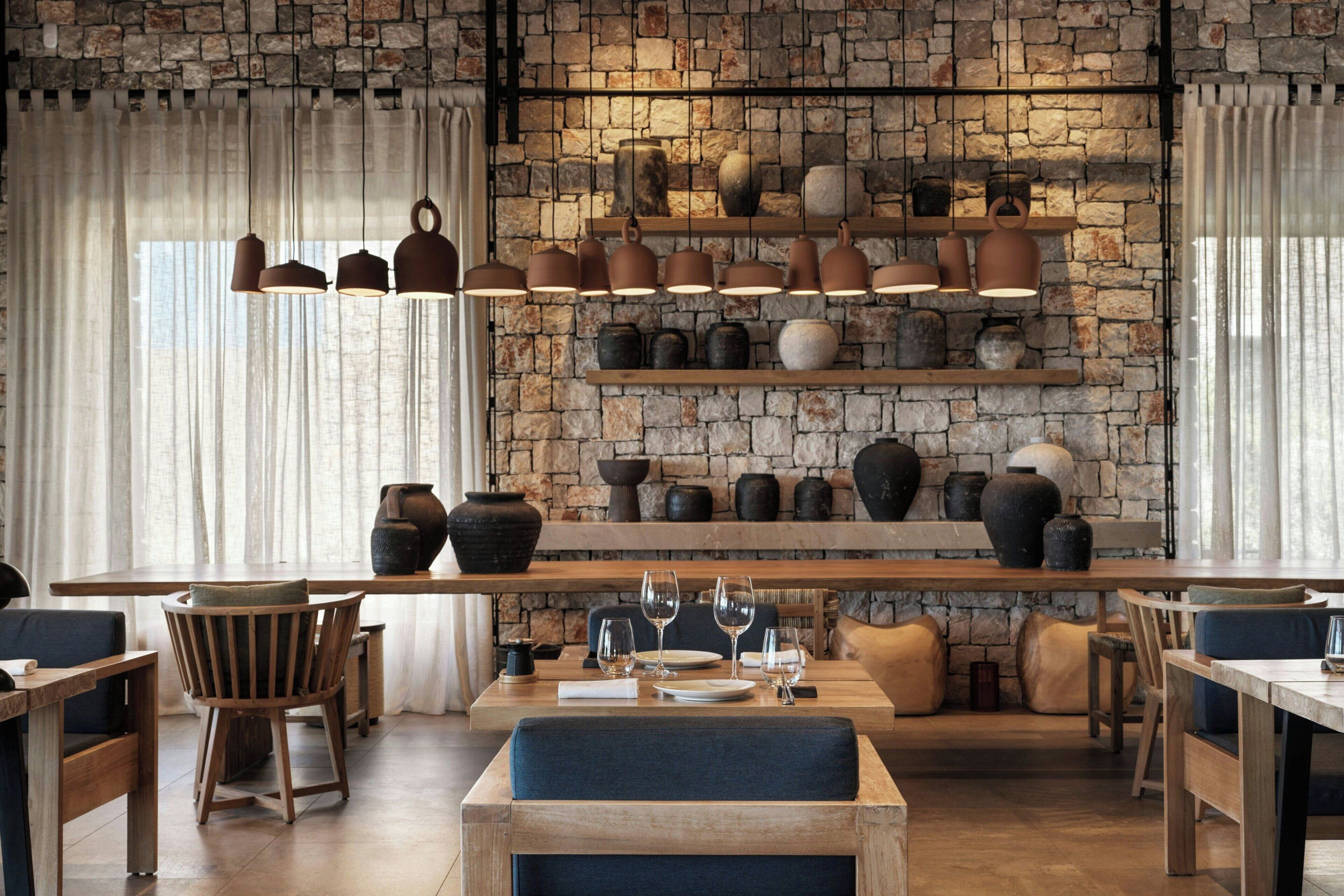 A restaurant with a rustic stone wall, wooden furniture, and hanging pottery.