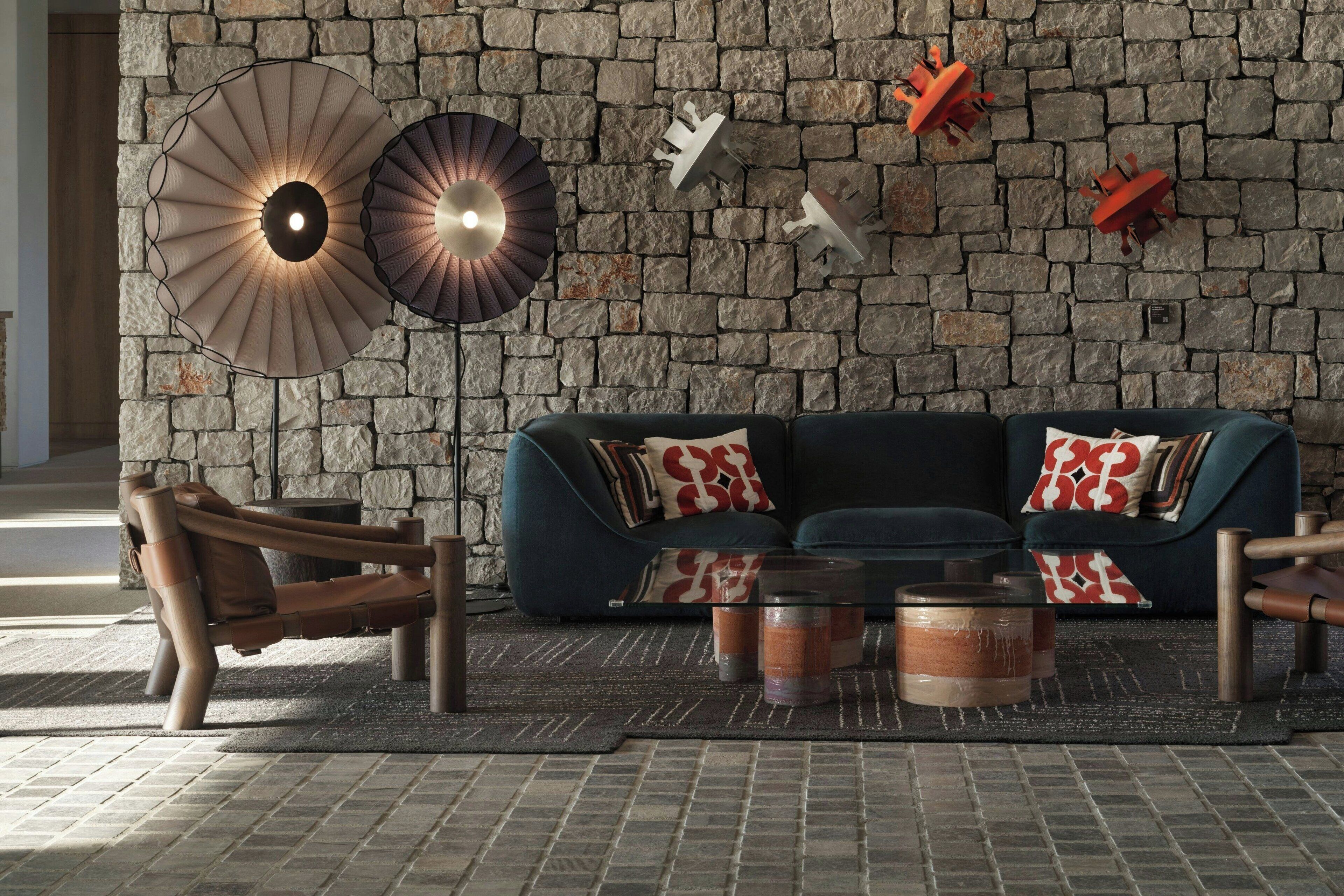 A modern living room with a stone wall, a dark blue sofa, wooden armchairs, and a coffee table with candles.