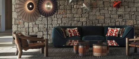 A modern living room with a stone wall, a dark blue sofa, wooden armchairs, and a coffee table with candles.