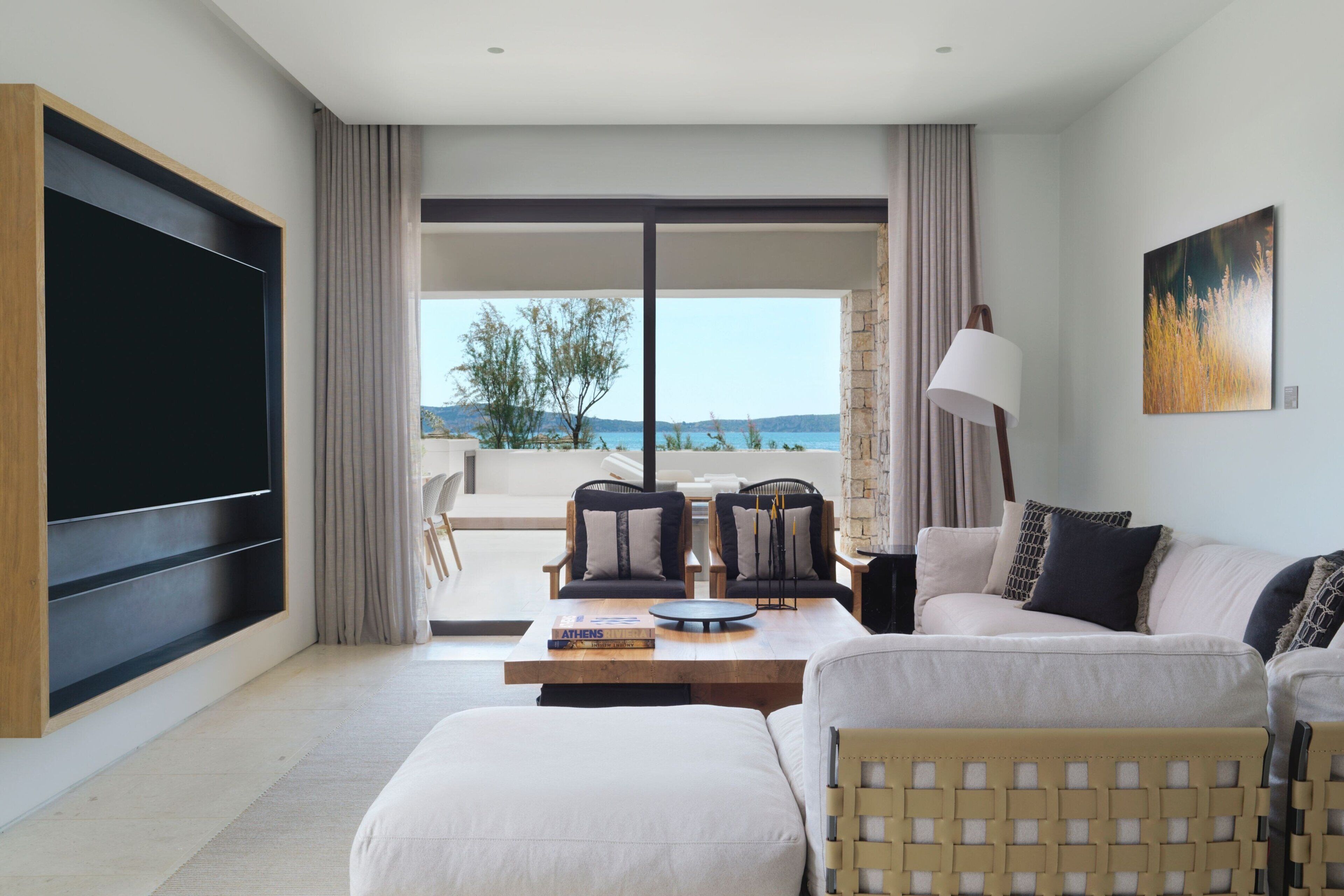 A modern living room with a large flat-screen TV, a sofa, a coffee table, and a view of the outdoors.