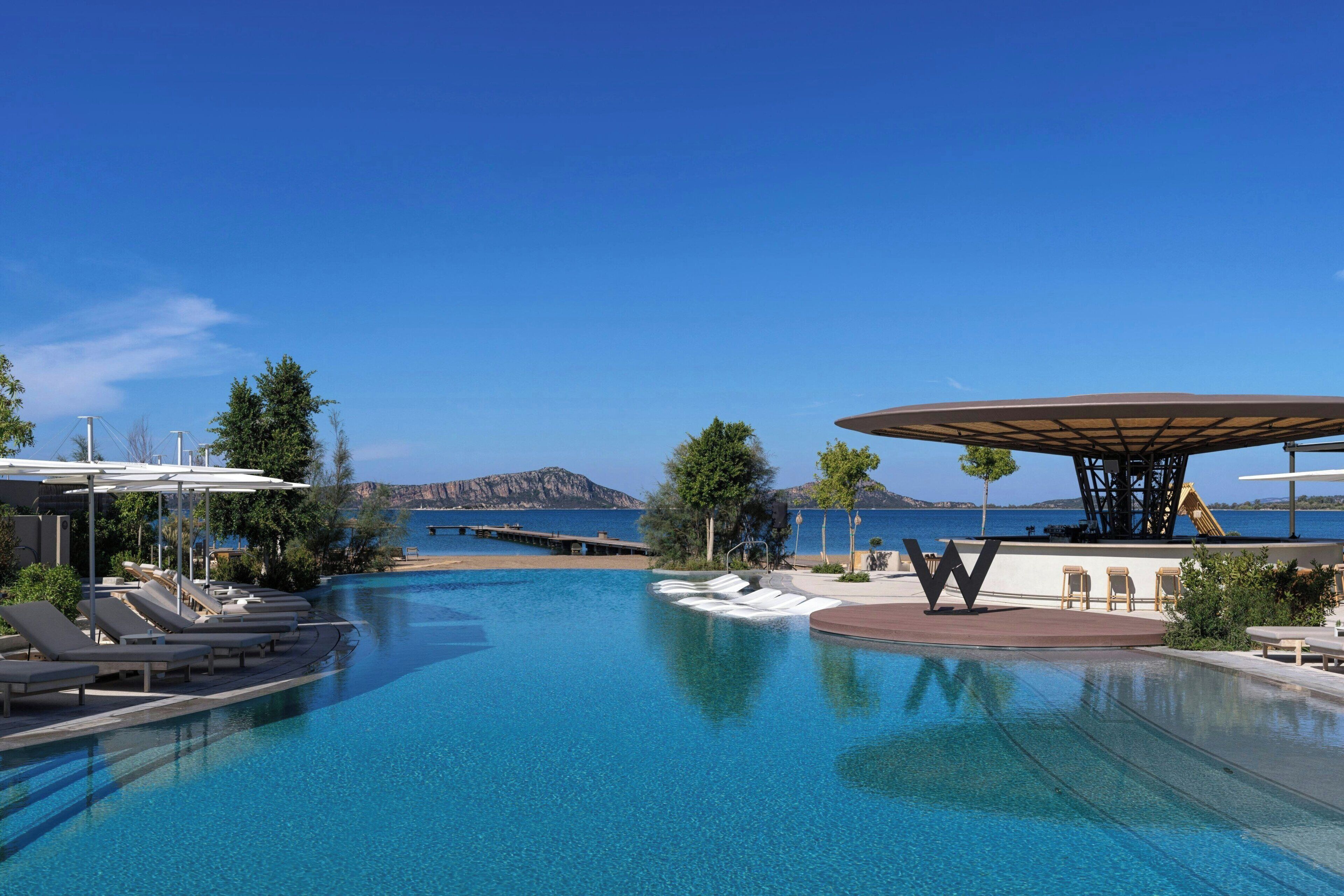 Une piscine d’eau cristalline, des chaises longues, un espace ombragé et une vue sur la mer et les montagnes.