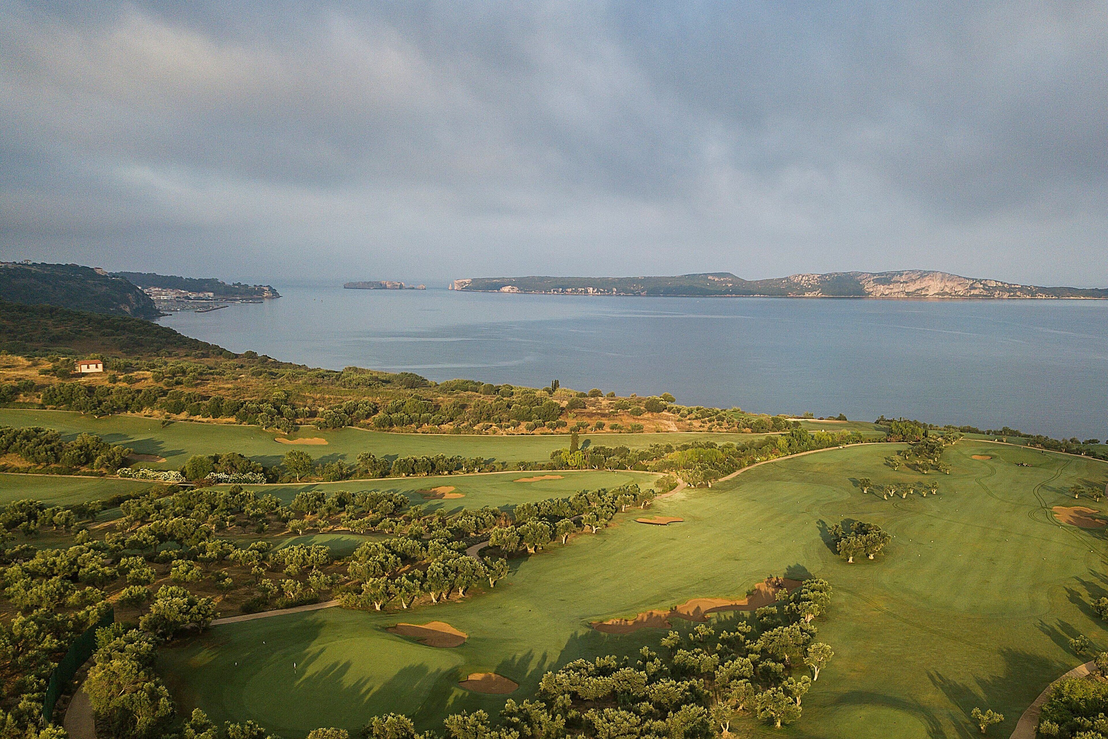 A golf course with a coastal view, including a lighthouse and distant mountains.