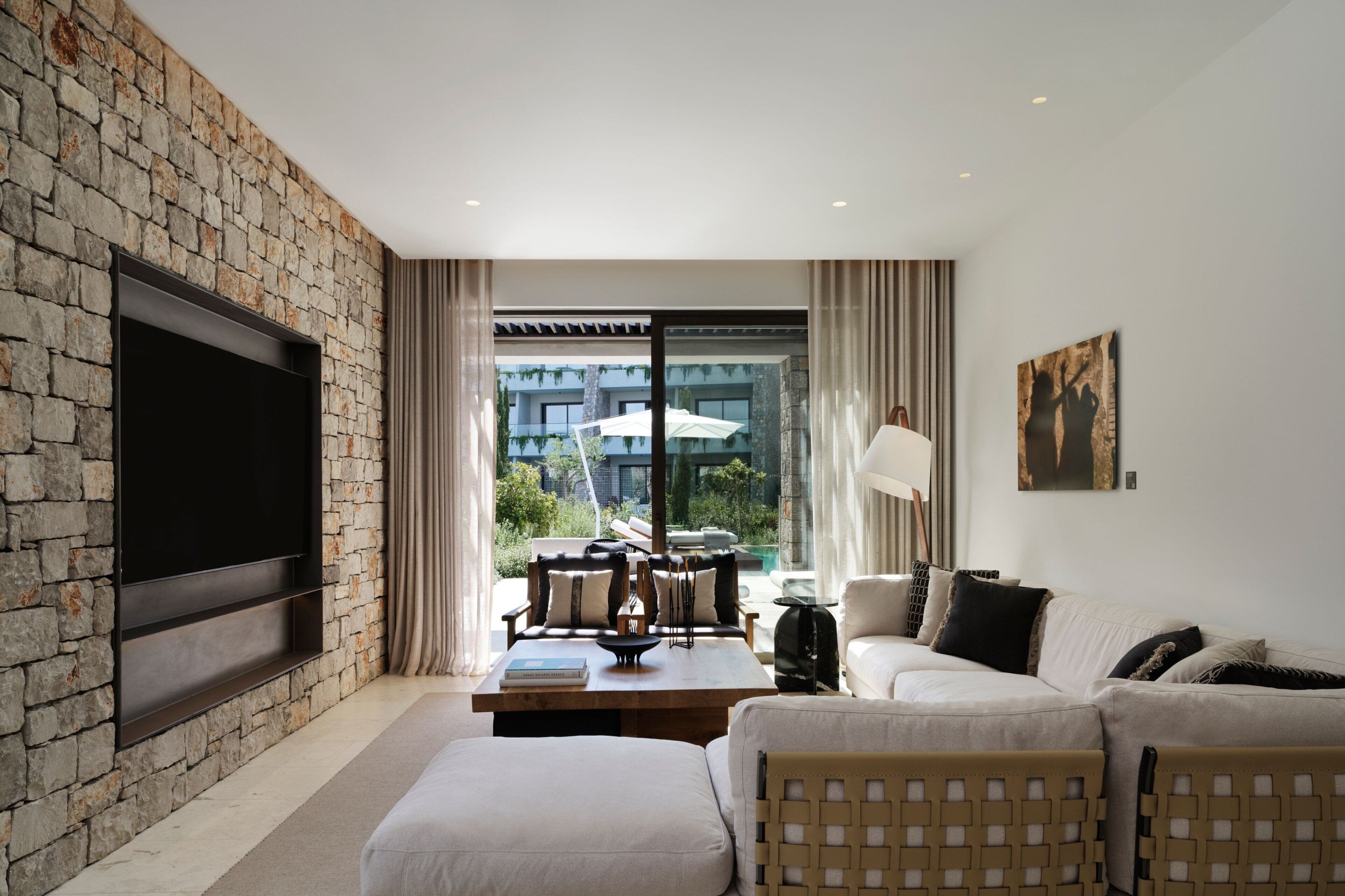 A modern living room with a stone wall, a flat-screen TV, a sofa, and a view of the outdoors.