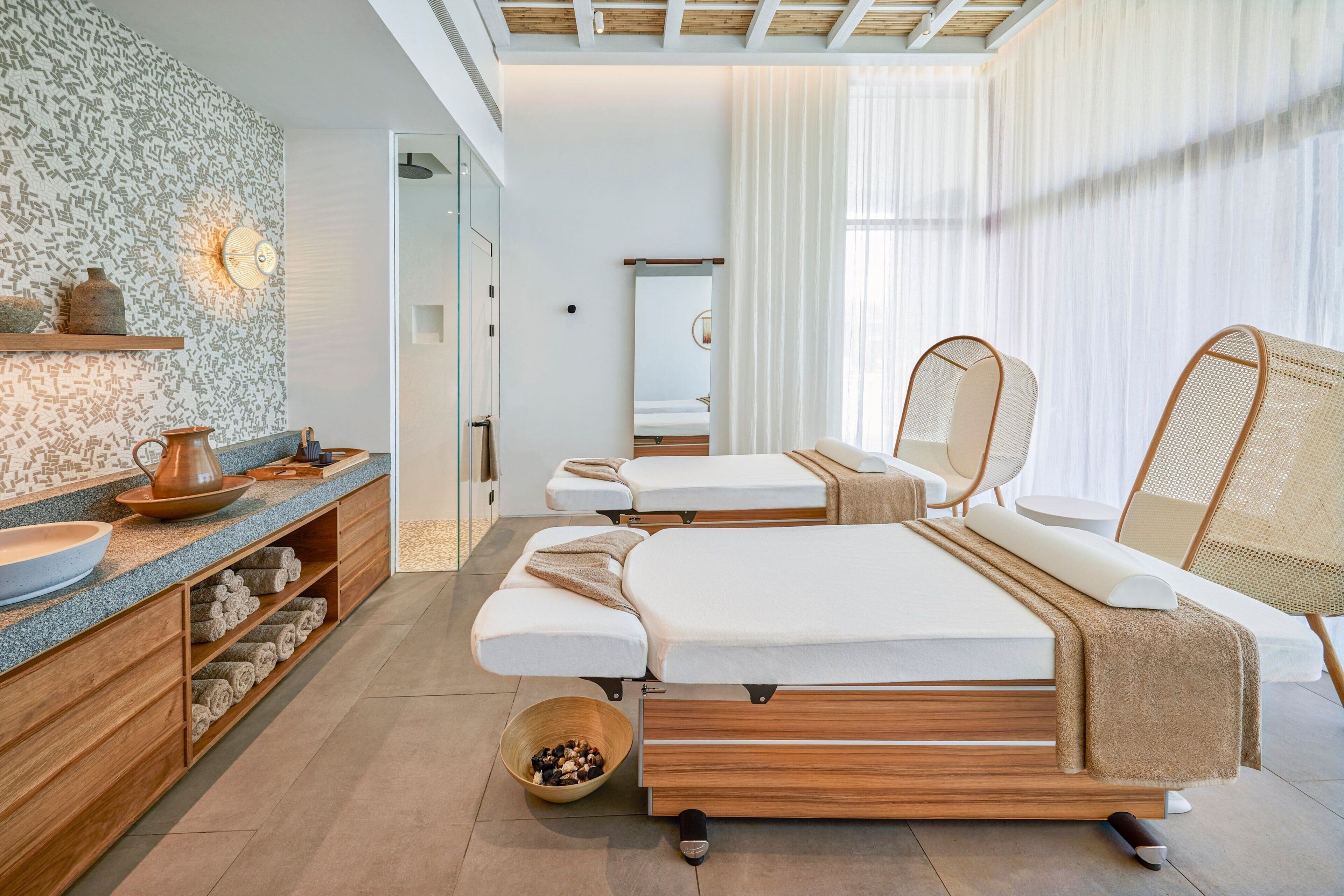 Une salle de spa moderne avec un lit en bois, une coiffeuse en bois dotée d’un lavabo en forme de coupe, et un grand miroir.