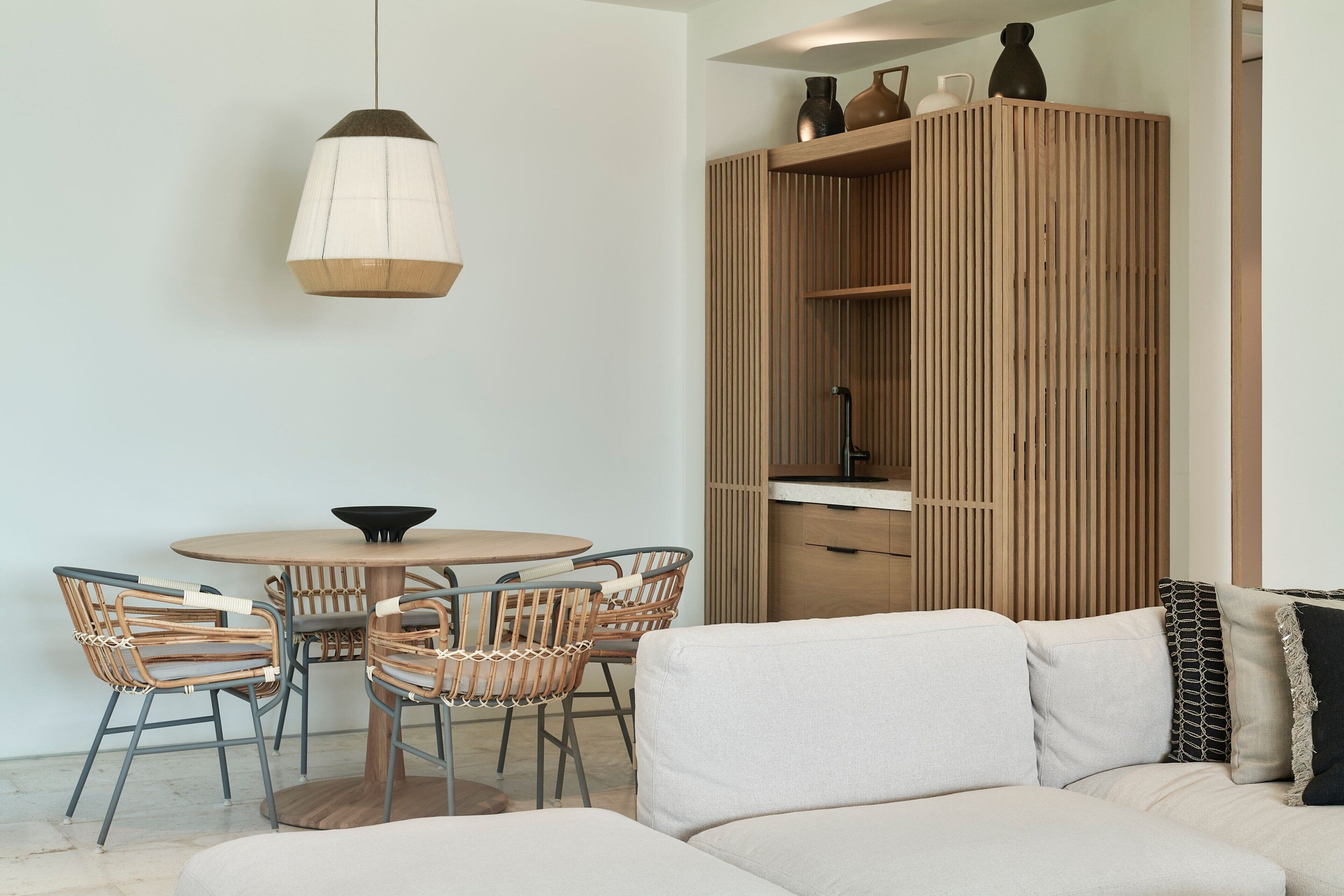 A modern living room with a round dining table, wicker chairs, a sofa, and a wooden cabinet.