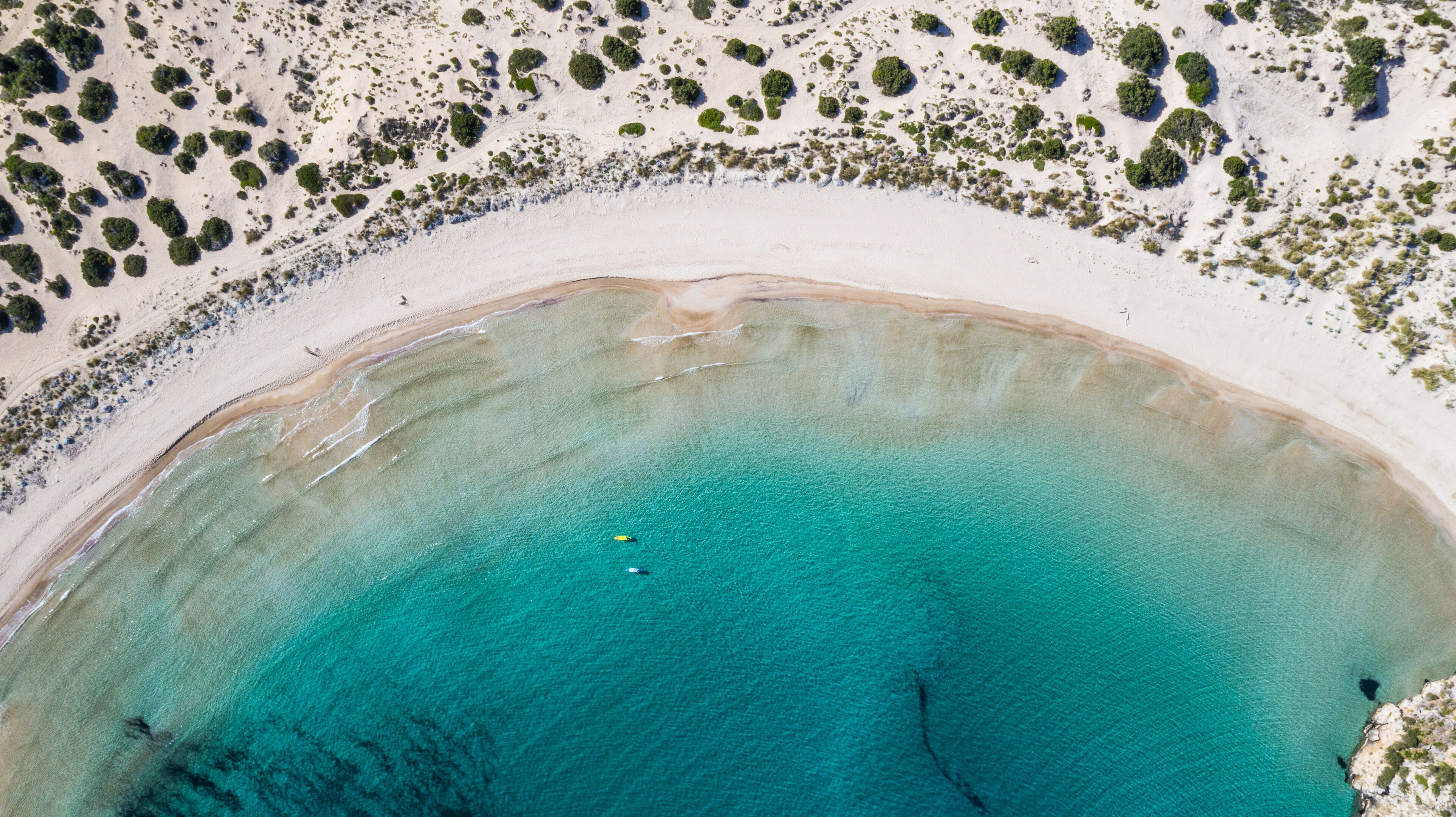 Vista aérea de una playa con aguas turquesas cristalinas y vegetación escasa.