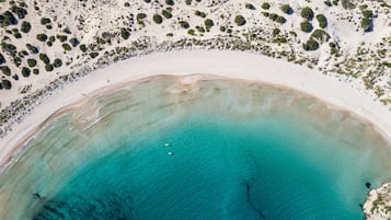 Vista aérea de una playa con aguas turquesas cristalinas y vegetación escasa.