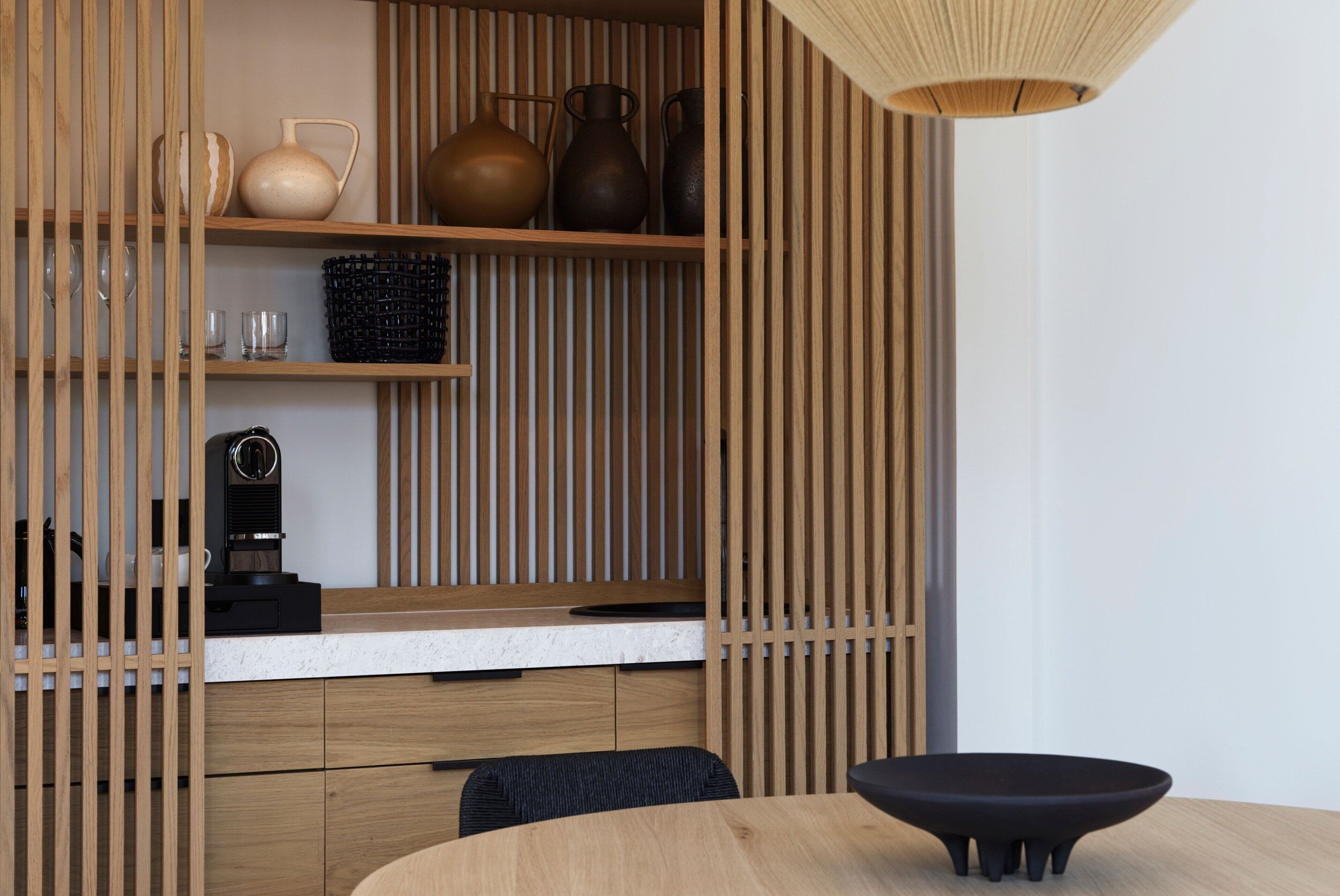 A modern kitchen with wooden cabinetry, a countertop, and a dining area with a round table and black chairs.
