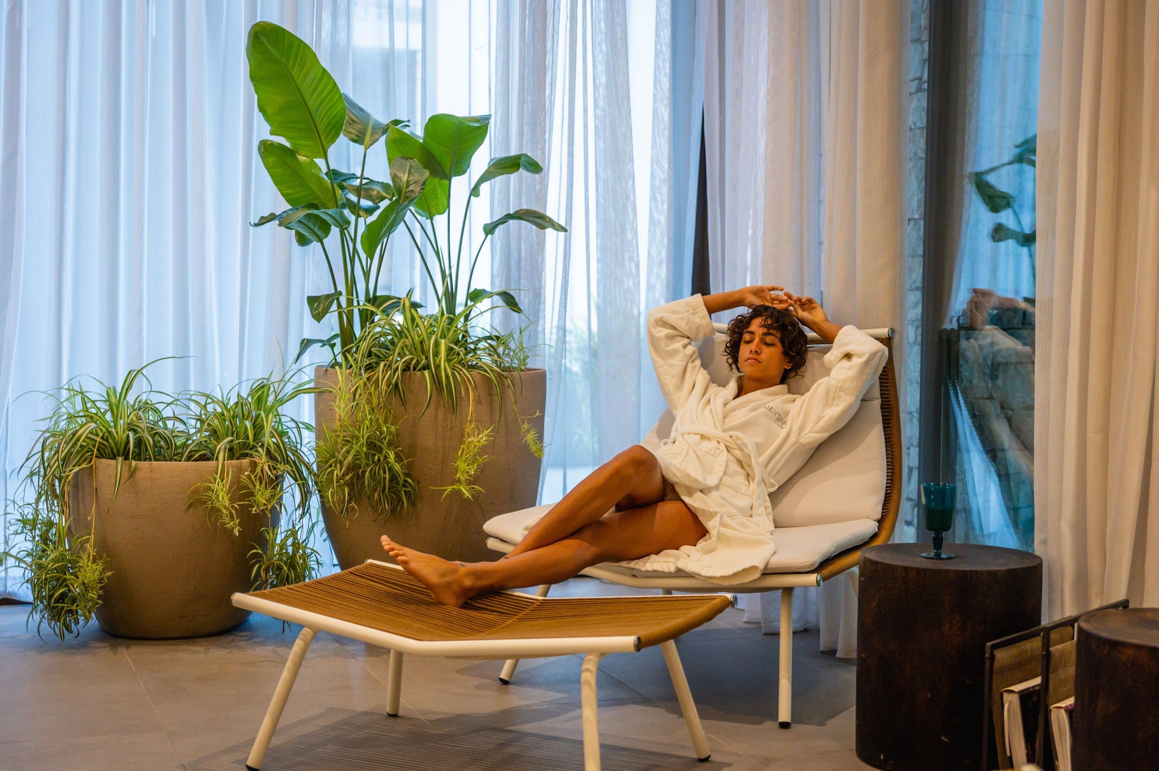 Une personne se détend dans un fauteuil, avec une grande plante en pot placée à côté d’elle.