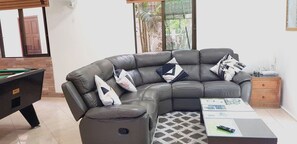 A living room with a sectional sofa, a pool table, and a small wooden side table.