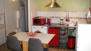 Una cocina funcional con microondas, cafetera y lavabo. Se observa un armario rojo, lavavajillas y una mesa con sillas.