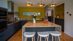 A modern kitchen with a central island, bar stools, pendant lighting, and a yellow accent wall. - Le Corentin        . (Concarneau)