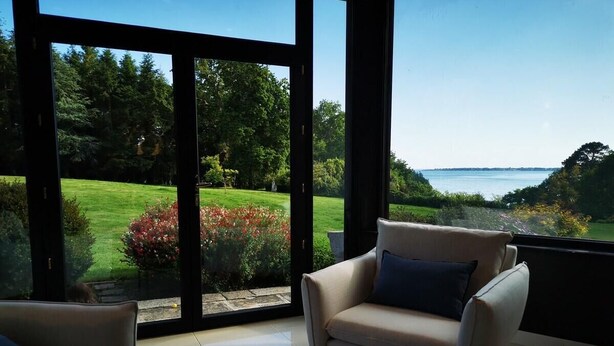 Ein modernes Wohnzimmer mit einem großen Glasschiebefenster, das in einen Garten mit Meerblick führt.