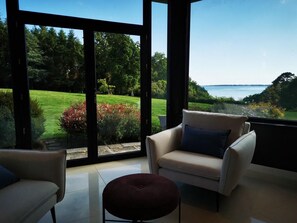 A modern living room with a large glass door leading to a garden and a view of the sea. - Le Marche-Avec     . (Concarneau)