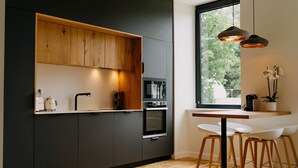 Una cocina moderna con armarios oscuros, encimera de madera y horno empotrado. Se ve una ventana con vistas a árboles.