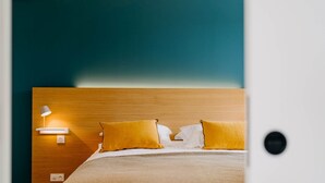 Una cama bien hecha con cabecera de madera, una lámpara de noche y dos almohadas.