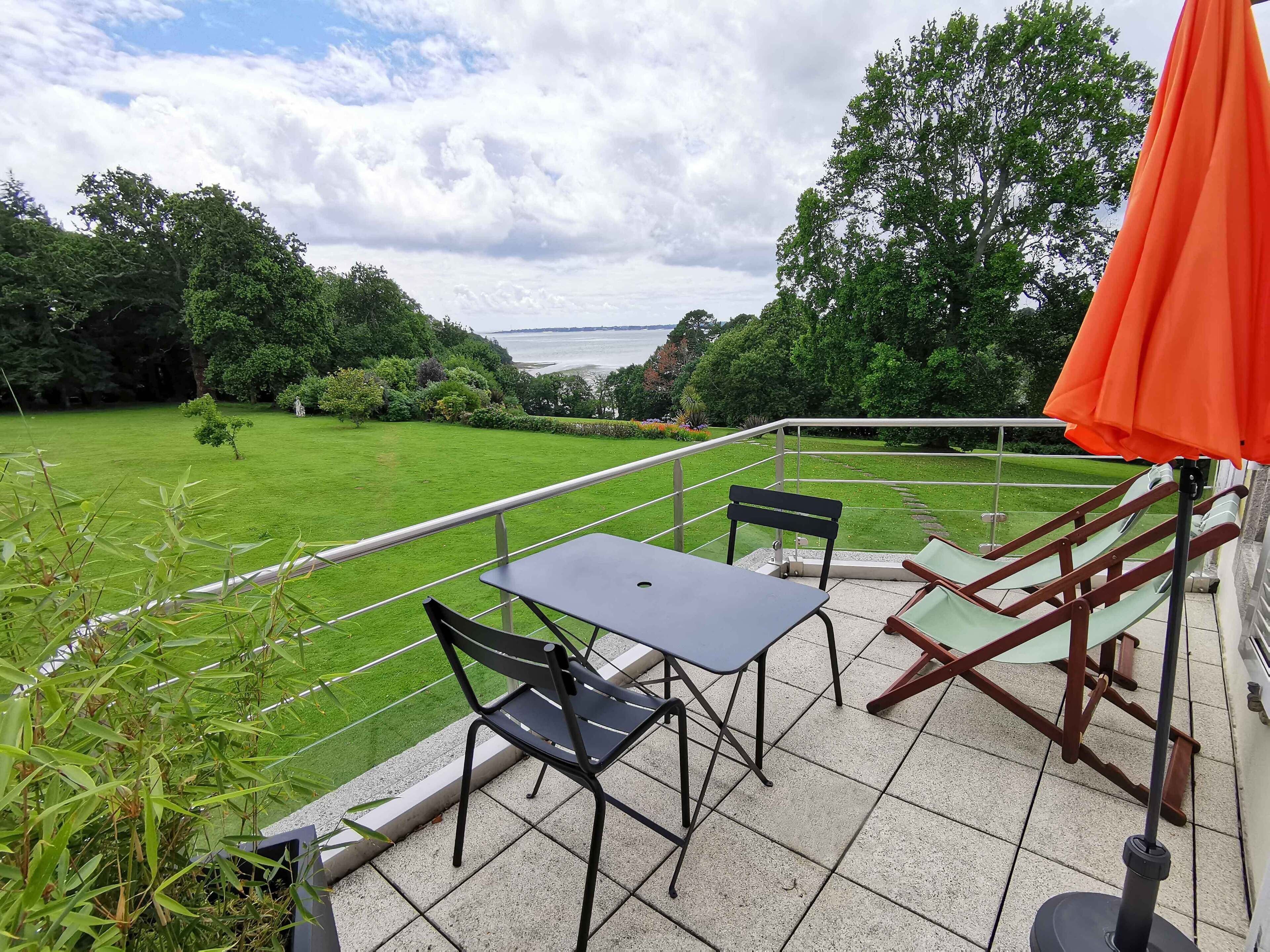 Une terrasse avec une table et des chaises, une balustrade et une vue sur une pelouse verdoyante et des arbres.