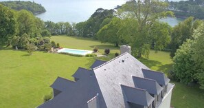 Une propriété résidentielle dotée d’une piscine, entourée d’une végétation luxuriante et offrant une vue sur un lac.