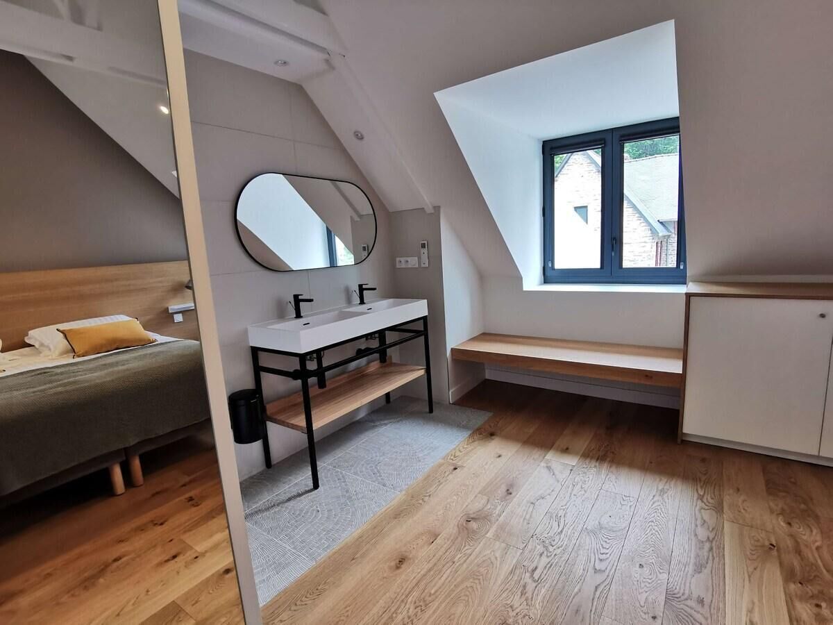 A modern bedroom with a loft bed, a vanity with a mirror, a small window, and a wooden floor.