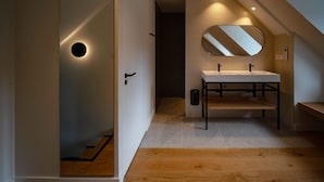 Un bany modern amb sòl de fusta, un lavabo blanc i un mirall gran.