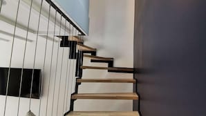 Una escala moderna amb graons de fusta i barana metàl·lica, que condueix a una paret fosca amb un llum circular.