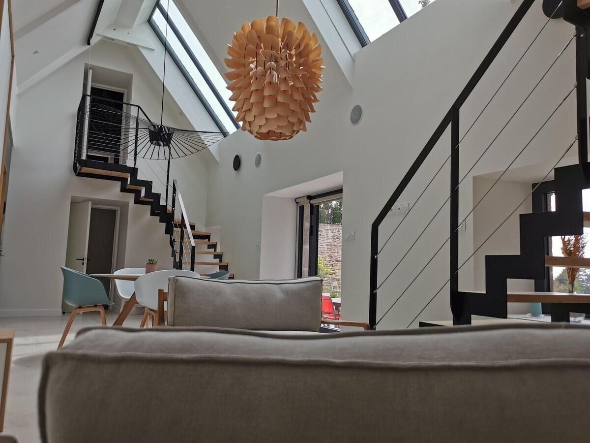 A modern living room with a staircase, a dining area, and a large window providing natural light.