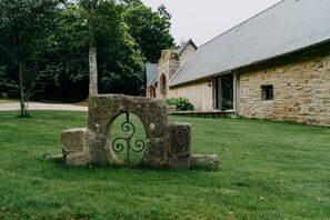 A stone structure with a decorative metal design in a grassy area with a stone building in the background.