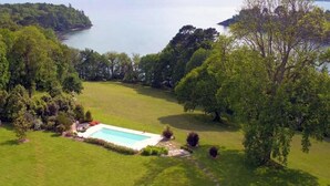 A large, open grassy area with a swimming pool surrounded by trees and hills in the background. - L'Etoile du Roy    . (Concarneau)
