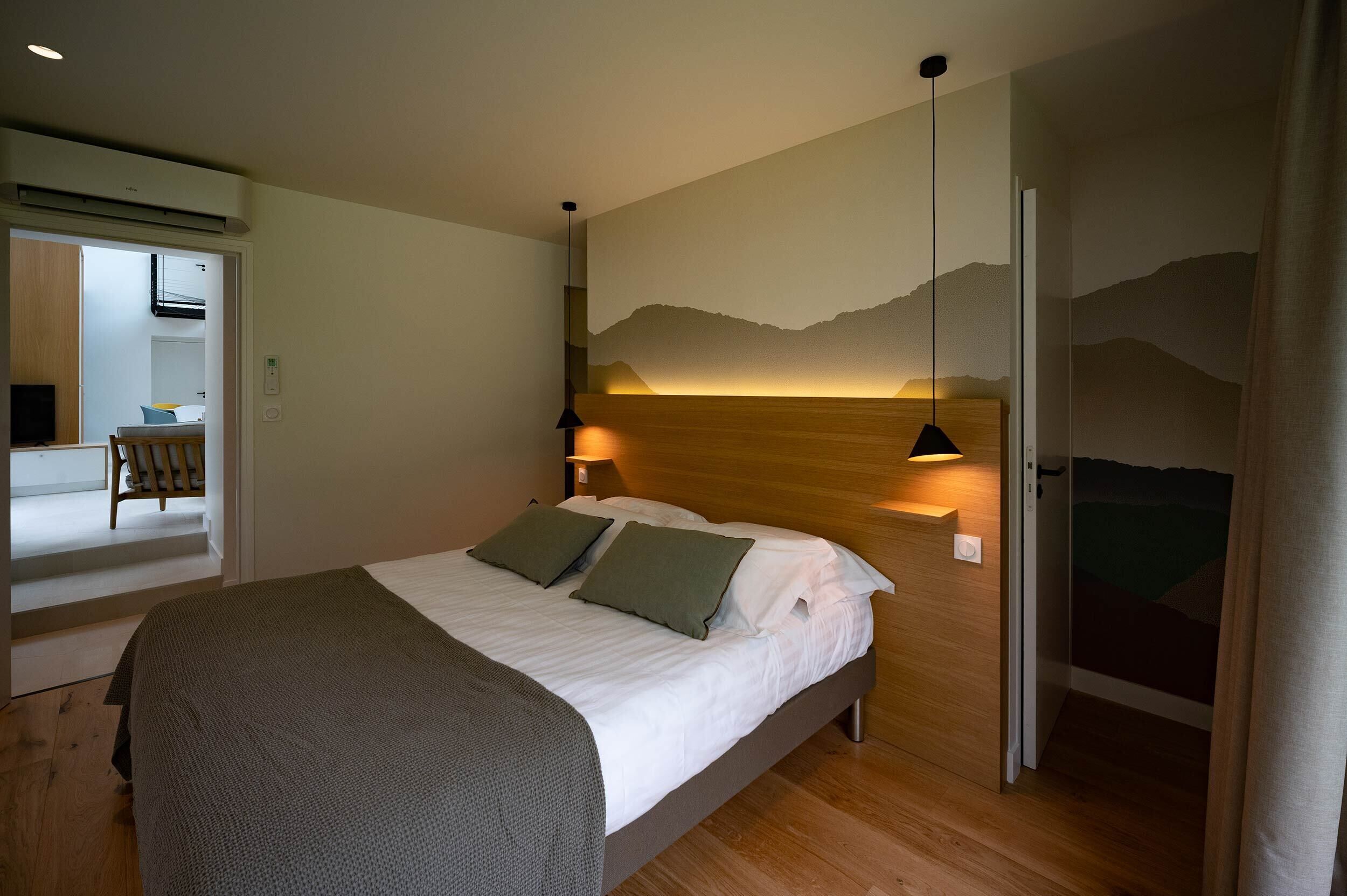 Een slaapkamer met een bed, een wandlamp en een deur naar een andere kamer.