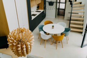 A modern dining area with a round table and chairs, a hanging light fixture, and a staircase.