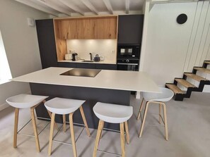 A modern kitchen with a central island, bar stools, and a staircase.