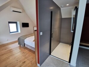 Une chambre moderne avec un plafond en pente, un lit intégré, une douche à l’italienne et une fenêtre laissant entrer la lumière naturelle.