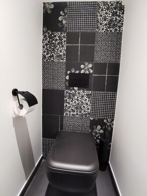 Une petite salle de bain moderne, équipée de toilettes, d’un porte-rouleau de papier toilette et d’un lavabo.