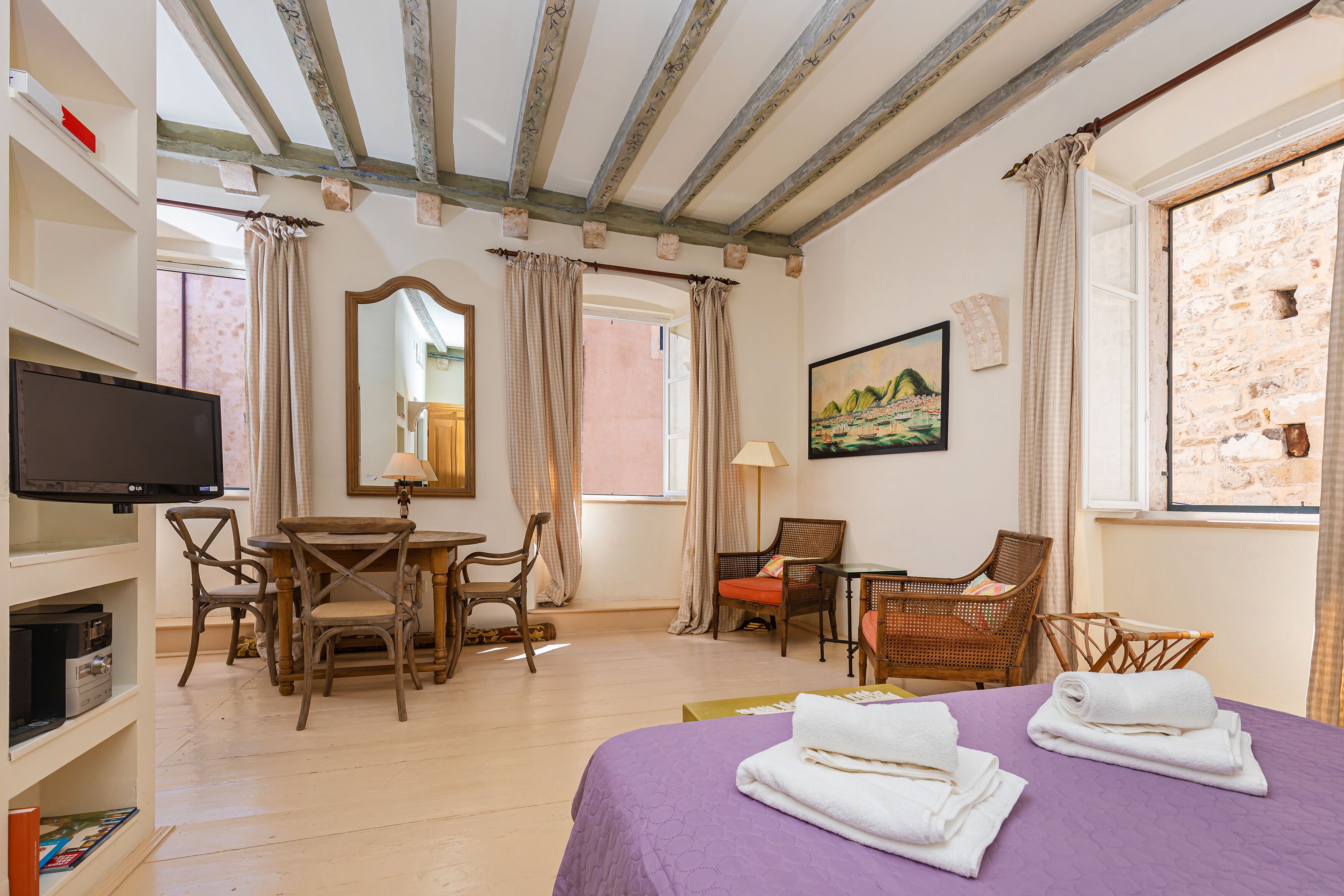 A hotel room with a bed, two chairs, a table, a TV, and a painting on the wall.