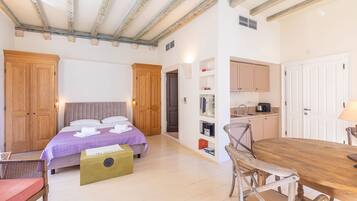 A bedroom with a bed, wooden wardrobe, bedside table, and a small kitchenette.
