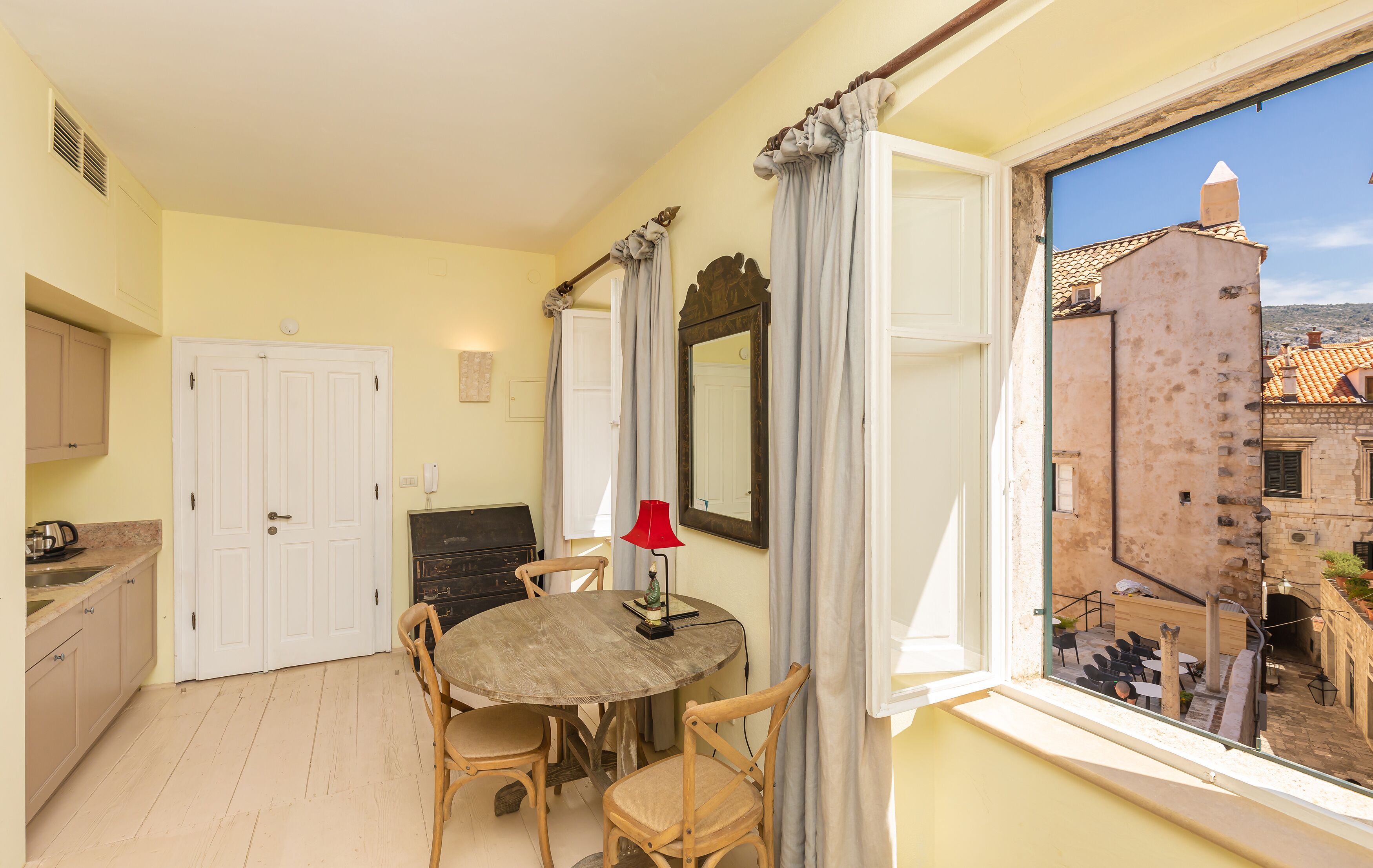 Una habitación con una mesa de comedor, sillas, una lámpara roja y una ventana con vistas a edificios.