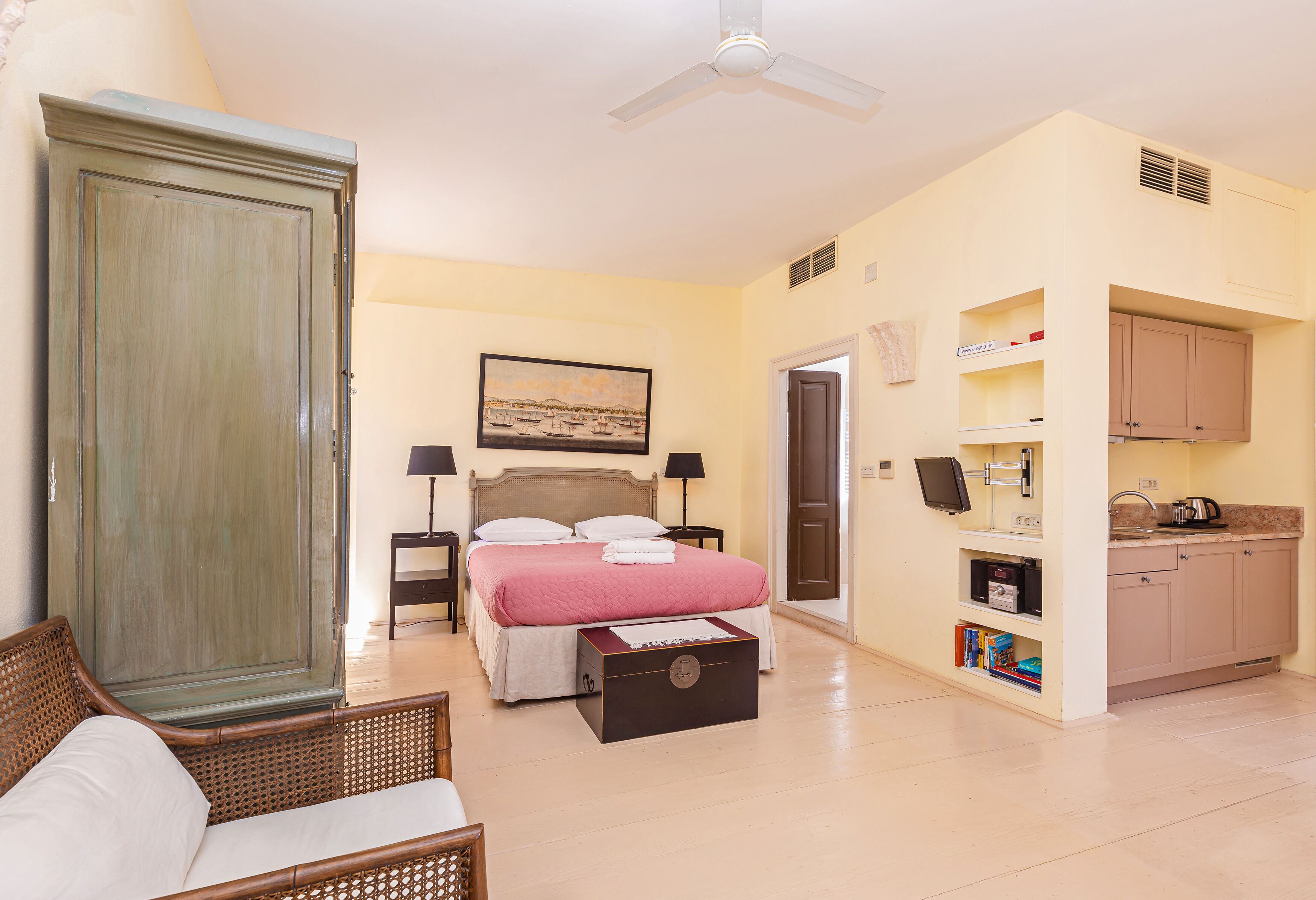 A bedroom with a bed, bedside tables, a wardrobe, a desk, and a kitchenette.