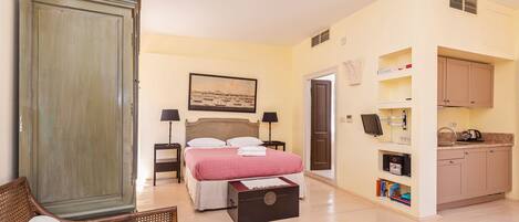 A bedroom with a bed, bedside tables, a wardrobe, a desk, and a kitchenette.