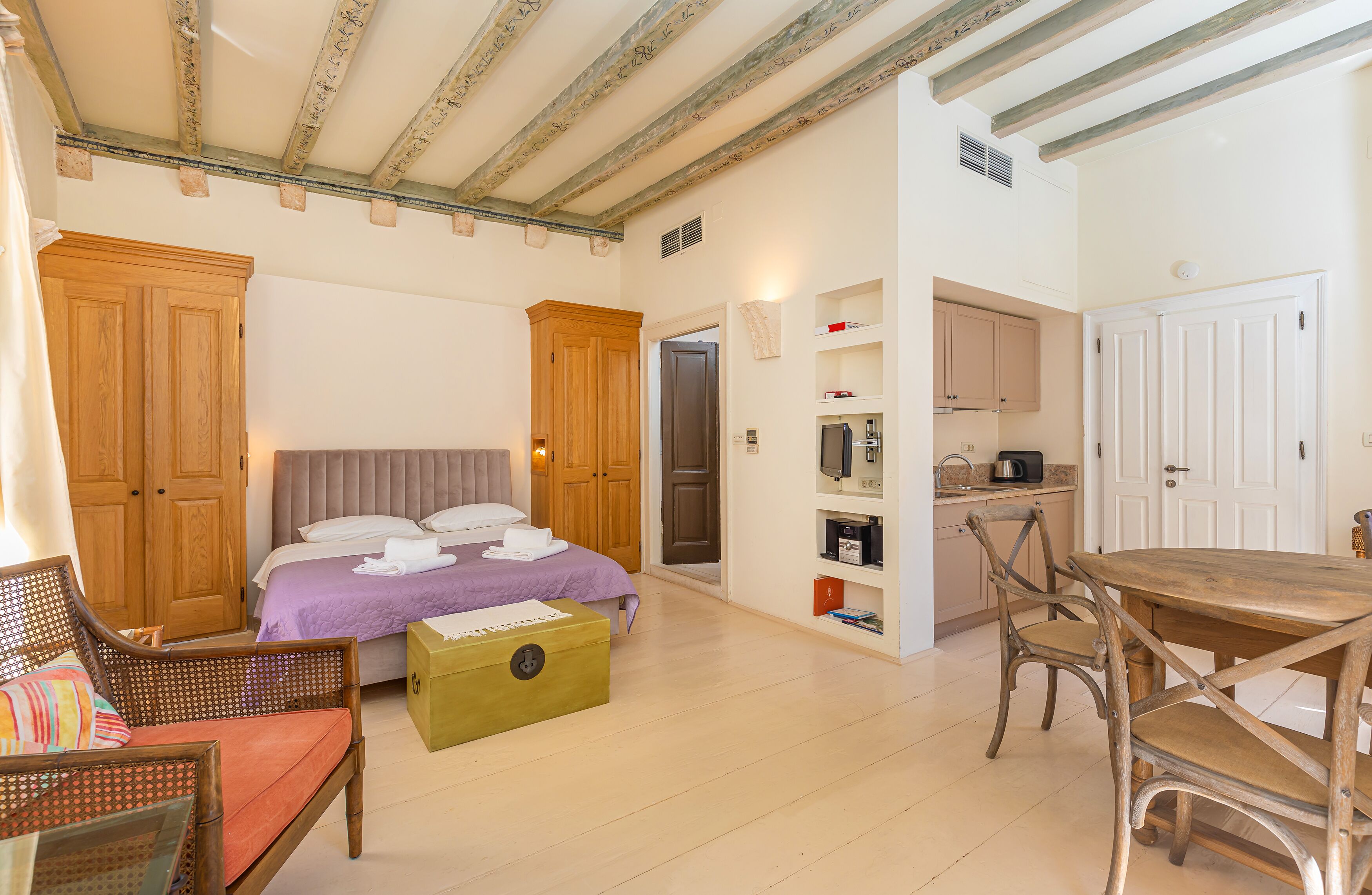 A bedroom with a bed, wooden wardrobe, and a small table with chairs.