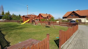 A playground with a yellow slide and swings, surrounded by a wooden fence, in a residential area with houses and a paved path. - Villa Leika - for families with a view of the Schneekoppe, dogs allowed (Mysłakowice)
