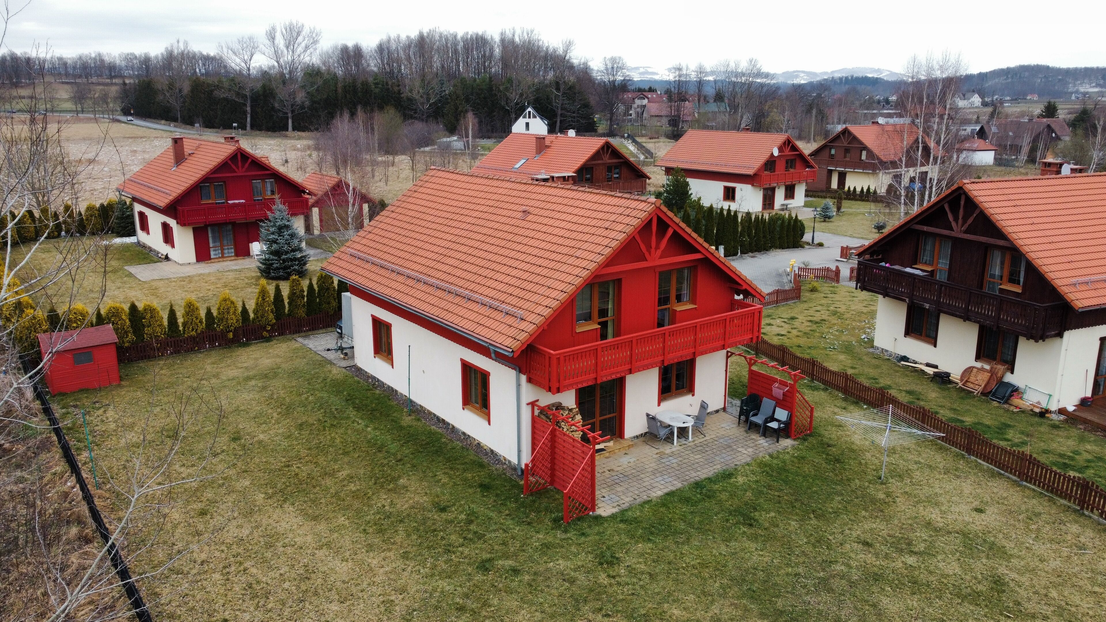 A residential area with multiple houses featuring red roofs and white walls, surrounded by a fenced yard and a small shed.