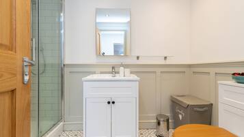 A bathroom with a shower, a sink with a mirror above it, a toilet, and a trash can.