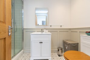 A bathroom with a shower, a sink with a mirror above it, a toilet, and a trash can. - Inviting 1-bed Apartment in Banbury (Banbury)